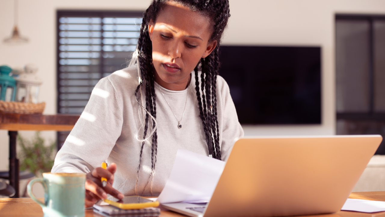 Woman sits in front of her computer doing calculations on a phone