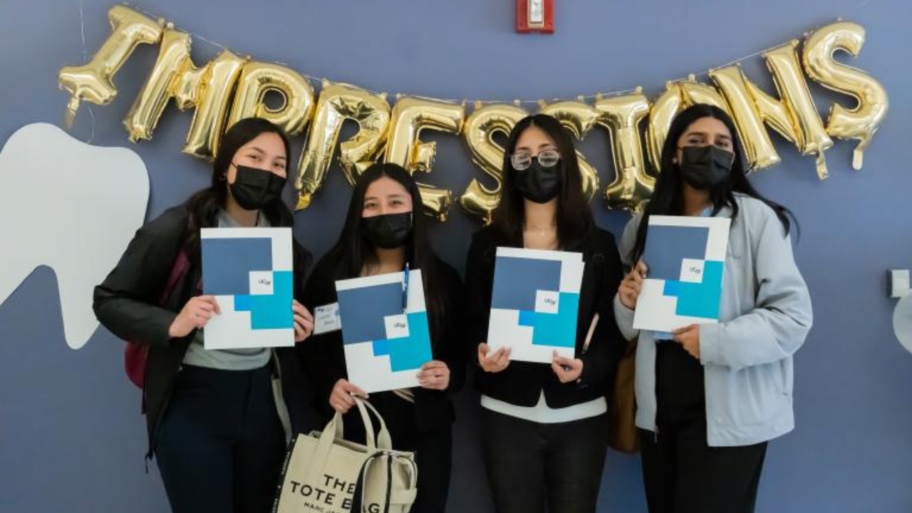 Students pose in front of a balloon banner that says "Impressions"