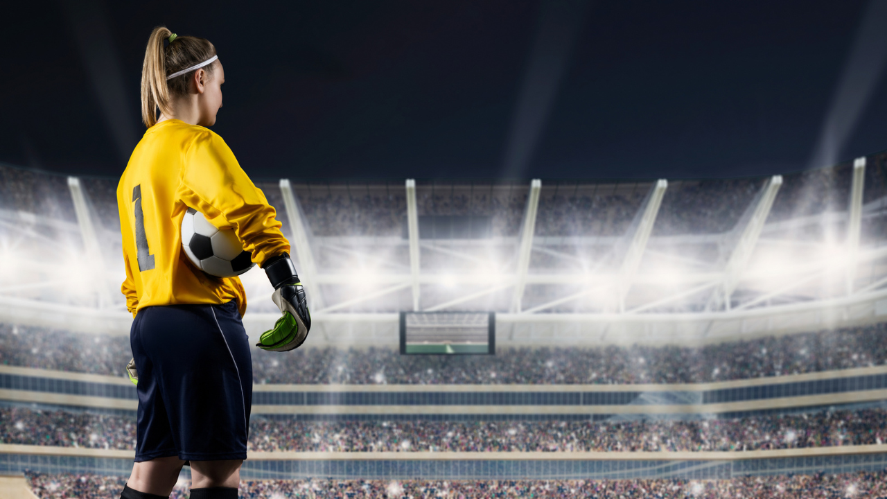 Female soccer player stands in a large stadium under stadium lights