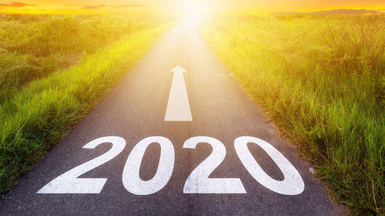 a paved road with "2020" in white paint on the pavement and an arrow pointing toward a rising sun