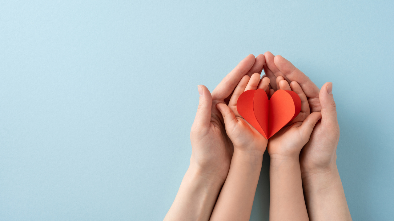 adult and child hands hold red paper heart cutouts