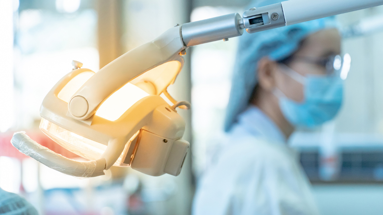 a dental chair light in the foreground with a dentist in the background