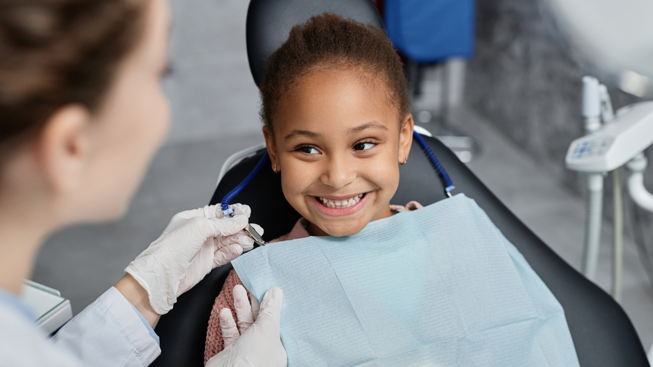 child in the dentist's chair looks up smiling at their dentist