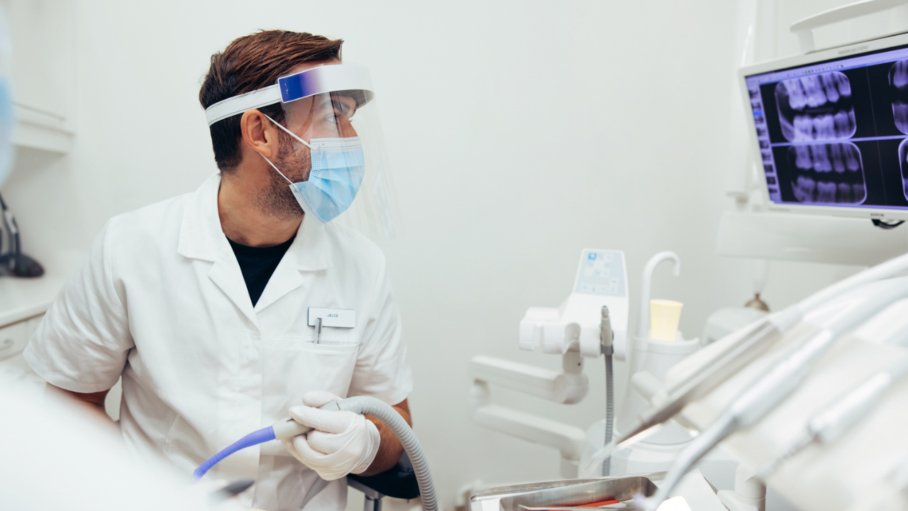 a dental provider wears a mask and face shield while looking at dental Xrays