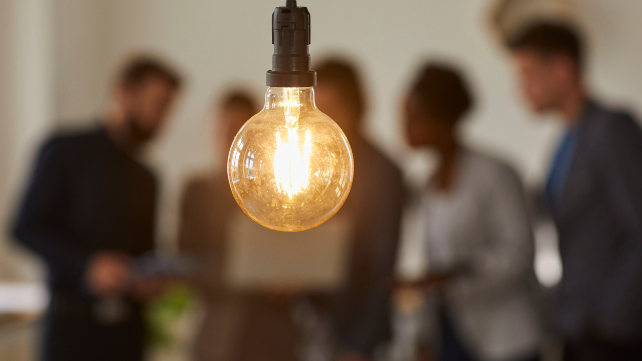 lightbulb in the foreground and a group of adults in conversation in the background
