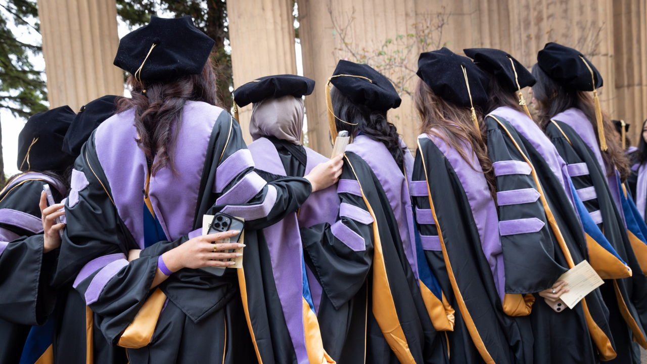 a group of UCSF School of Dentistry graduates stand together in their graduation regalia, facing away from the camera