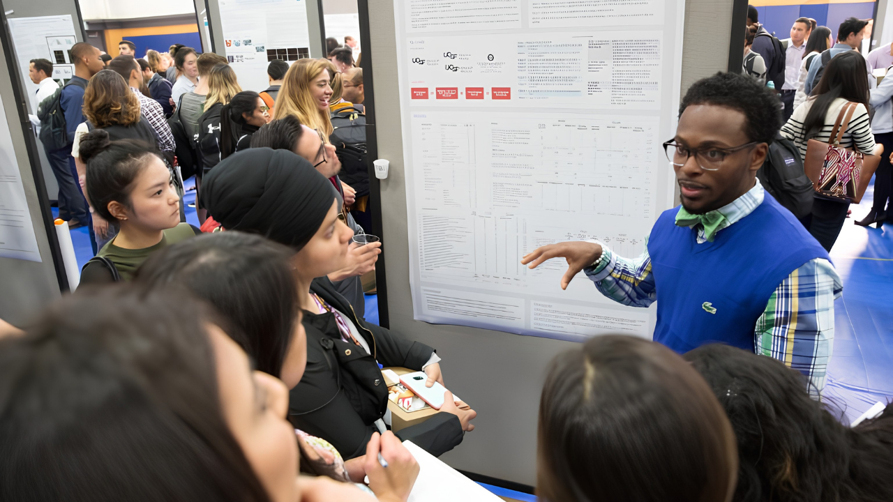Devon Cooper, DMD (right, in blue vest), discusses his research poster at Research and Clinical Excellence Day.