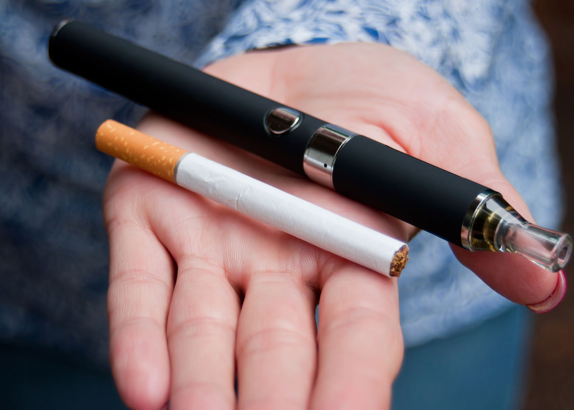 an open hand holding a cigarette and a vape