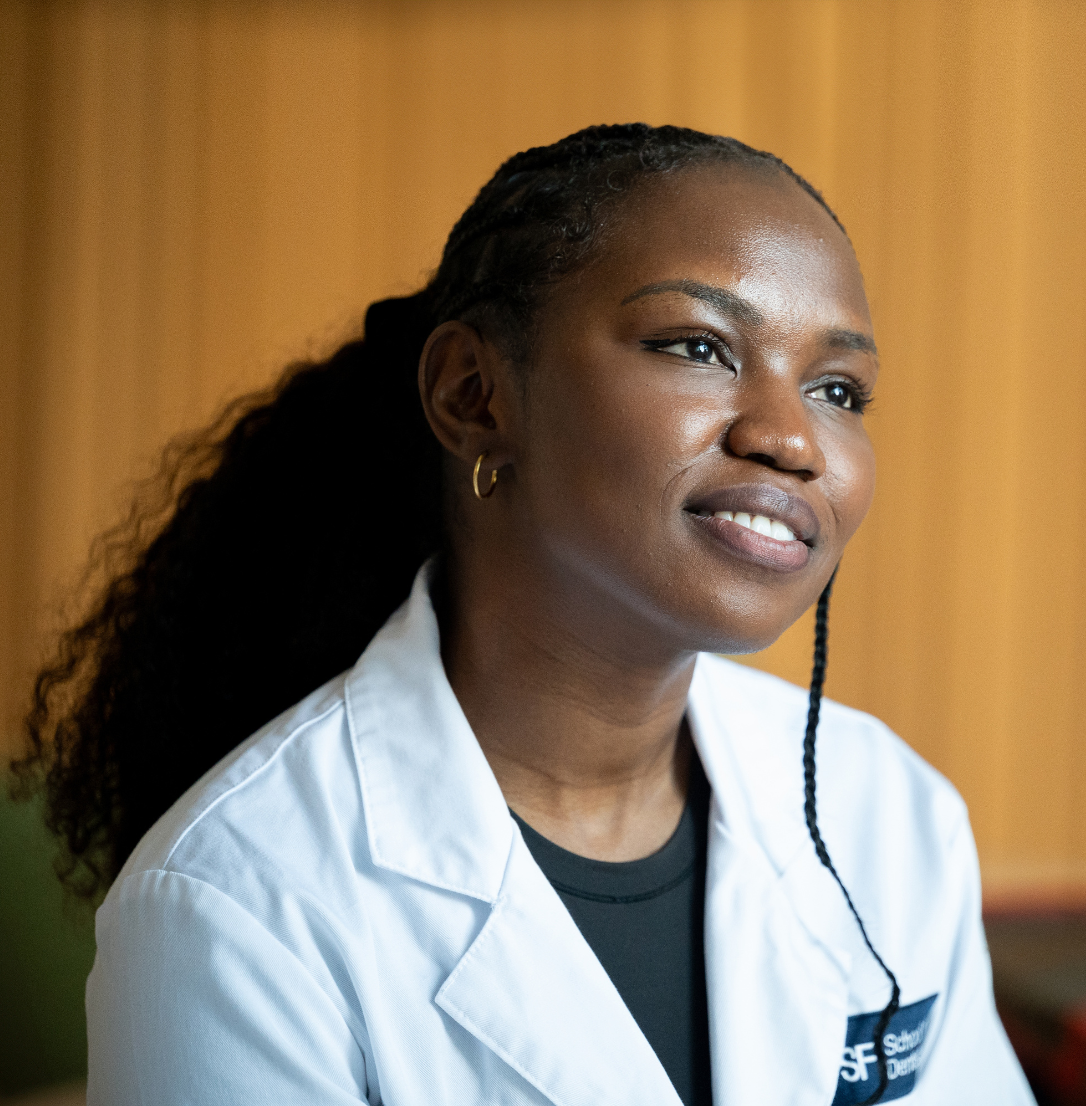 A smiling woman in a white dentist's coat smiles to the right of the camera