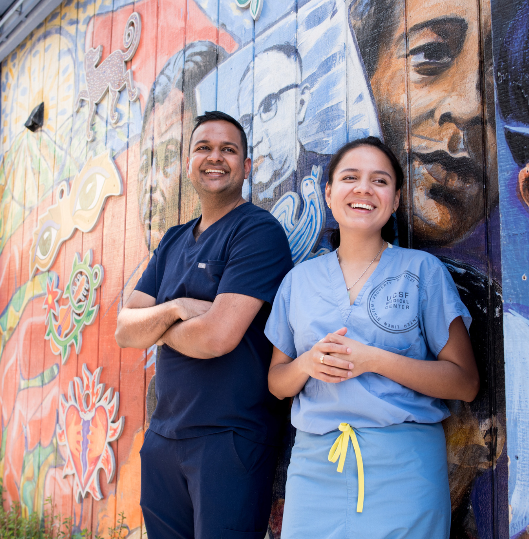Two dental students stand outside with a mural in the background