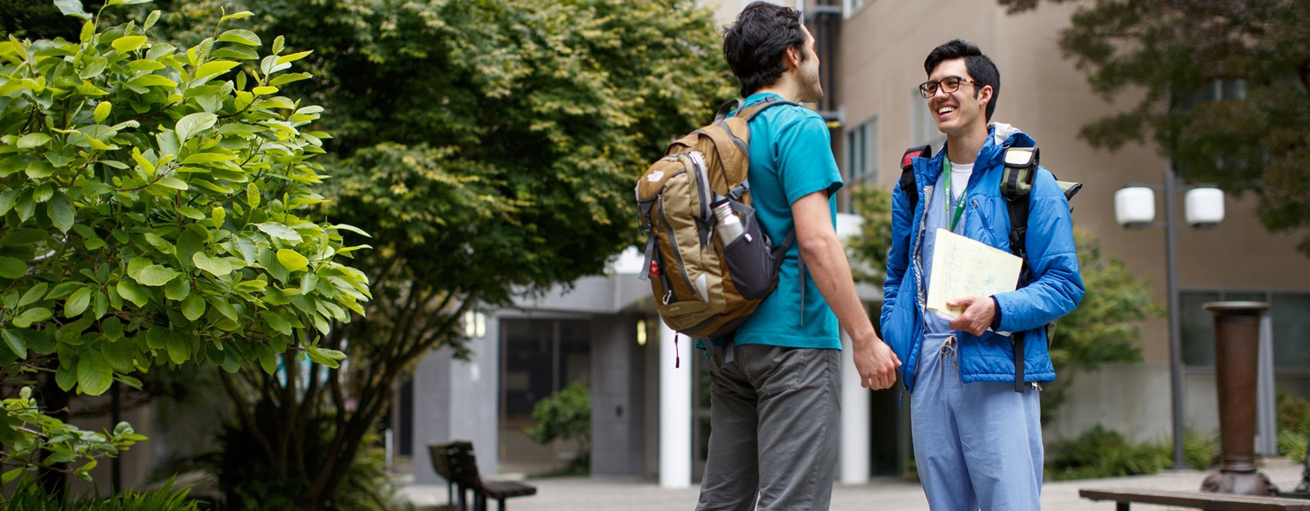 Two male students with backpacks talking and laughing outside on a campus.