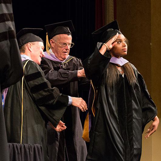 Jasmine Thomas salutes as Drs. James Giblin and Richard Mogensen adjust her hood.