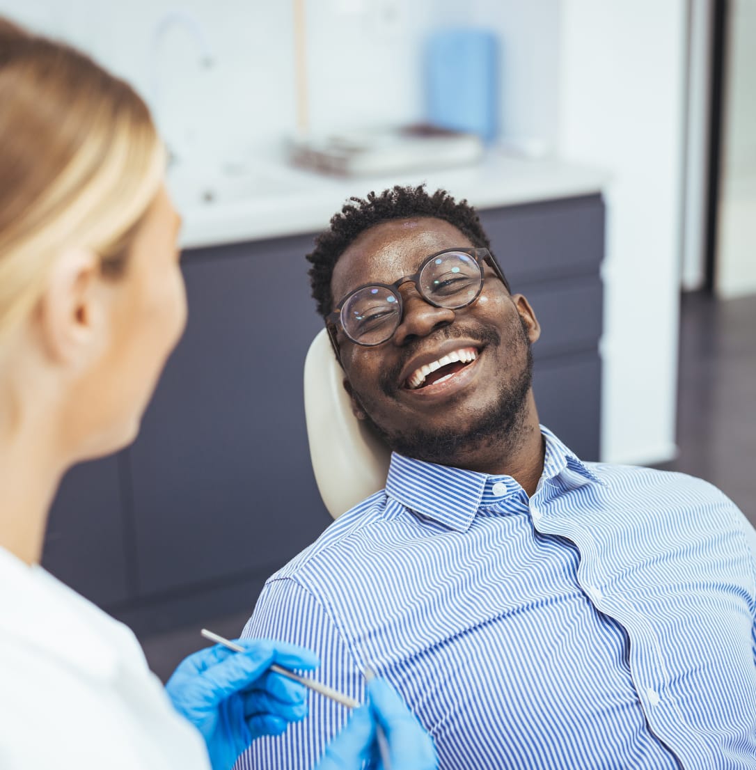 Woman dentist facing smiling man patient sitting in an exam chair in a clinic setting.