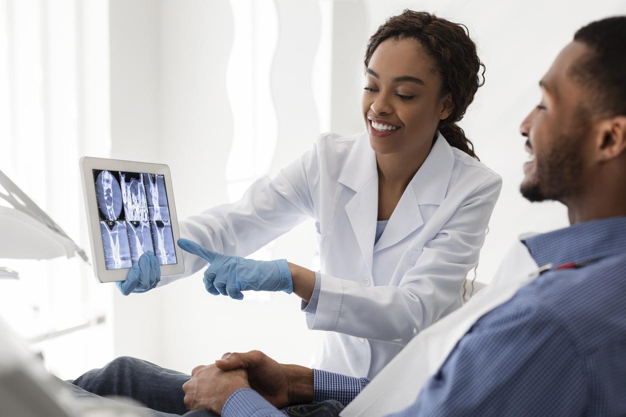 Smiling african female dentist showing patient teeth xray stock photo